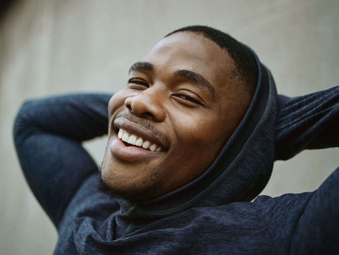 Happy Black man in a hoodie, head tilted back, hands behind head, smiling. Exploring favorite things about Black people.
