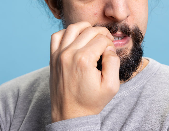 A man with a beard, wearing a grey sweatshirt, biting his fingernails, showing a gross office story.