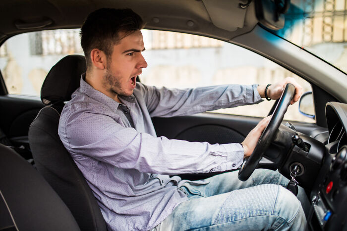 Young man showing frustration while driving a car, illustrating diverse forms of karma in satisfying moments.