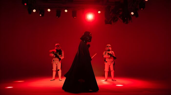 Darth Vader and two stormtroopers under red stage lights representing iconic 80s and 90s villains for a themed quiz. Darth Vader and two stormtroopers under red stage lights representing iconic 80s and 90s villains for a themed quiz.
