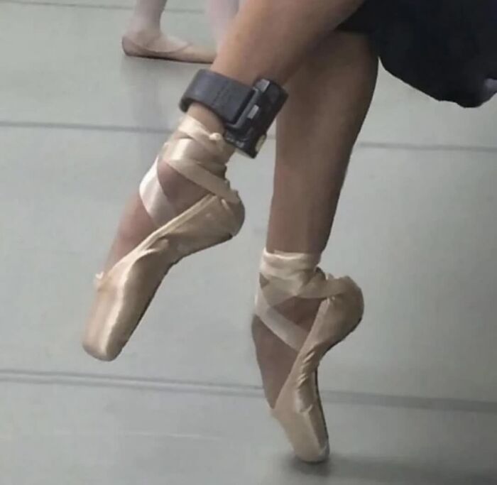 A ballerina's feet in pointe shoes, with an ankle monitor visible, making for a weird image.
