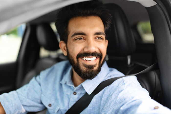 Smiling man wearing a blue shirt sitting in a car, representing bachelor and bachelorette party moments and experiences.