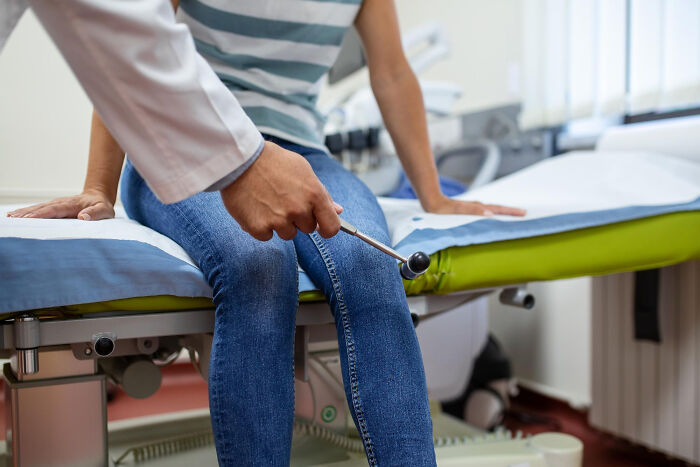 Doctor using a reflex hammer to check knee response during a body exam in a medical office setting