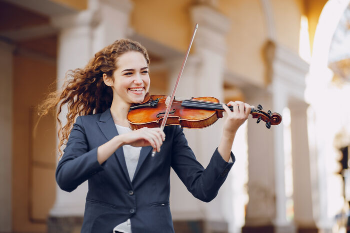 Young woman smiling while playing violin outdoors, illustrating random life decisions leading people to the right place.