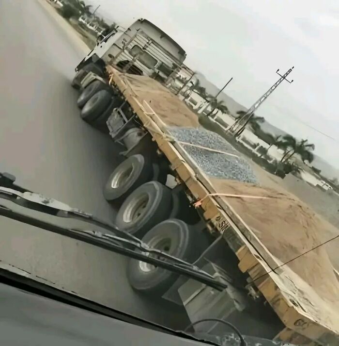 A weird image of a flatbed truck on the road, carrying both sand and gravel. People will go hmmm at this unusual sight.