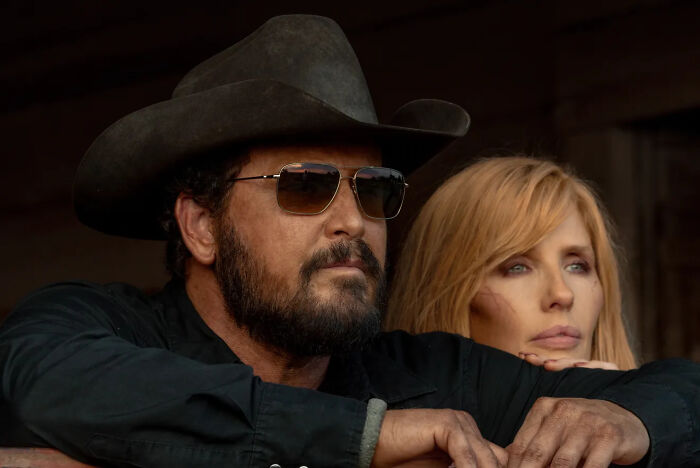 Rip and Beth of Dutton Ranch in black shirts and a cowboy hat, looking intently at something off-camera.