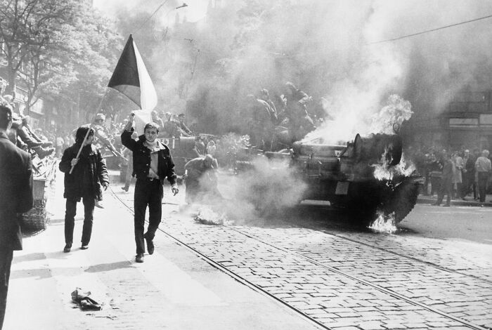 Protesters walking beside a burning tank during a historic 1960s demonstration, reflecting events in the year you were born.