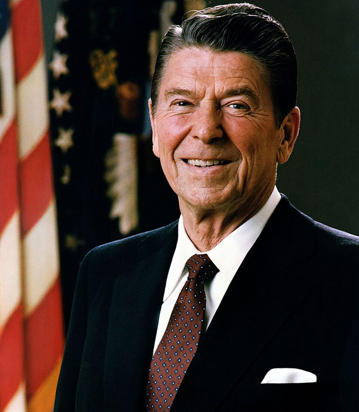 Portrait of a smiling man in a suit with an American flag in the background, representing massive betrayals in history.