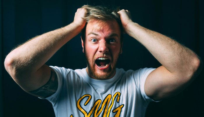 Frustrated man with beard holding head, expressing stress and anger related to things women are tired of explaining to men.