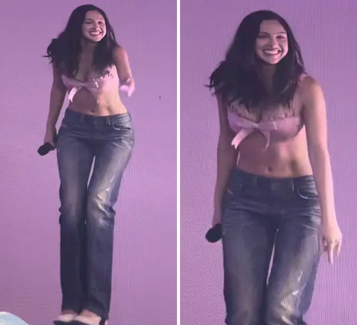 Young woman wearing a pink crop top and distressed jeans, smiling and holding a microphone at a festival fashion event.