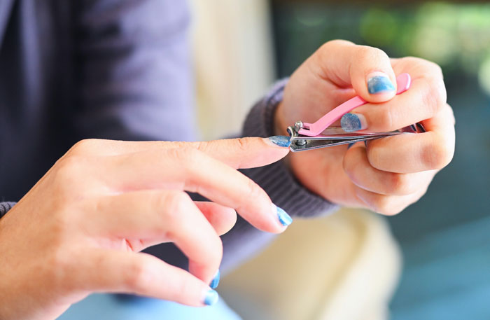 A person clipping a fingernail with a nail clipper, their nails painted blue, illustrating gross office stories.