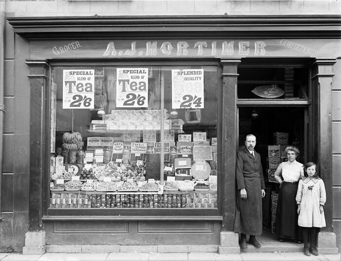 Black and white photo of a rare and interesting vintage grocery store with family posing outside the shop window.