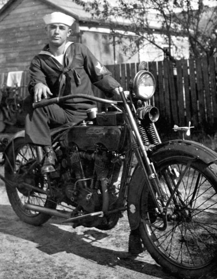 Vintage black and white photo of a sailor posing on an old motorcycle, rare and interesting historical image.