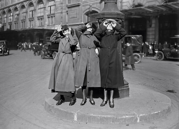 Three women in long coats using binoculars outdoors in a rare and interesting photo from a past time.