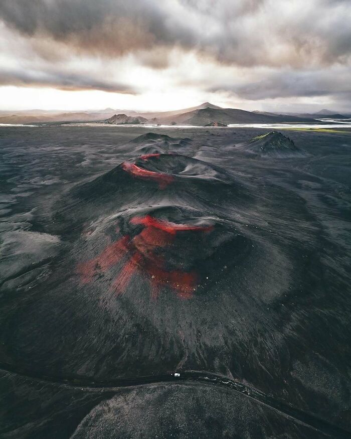 Unbelievable photos of volcanic landscape with dark craters and red lava, under a dramatic sky, like another universe.