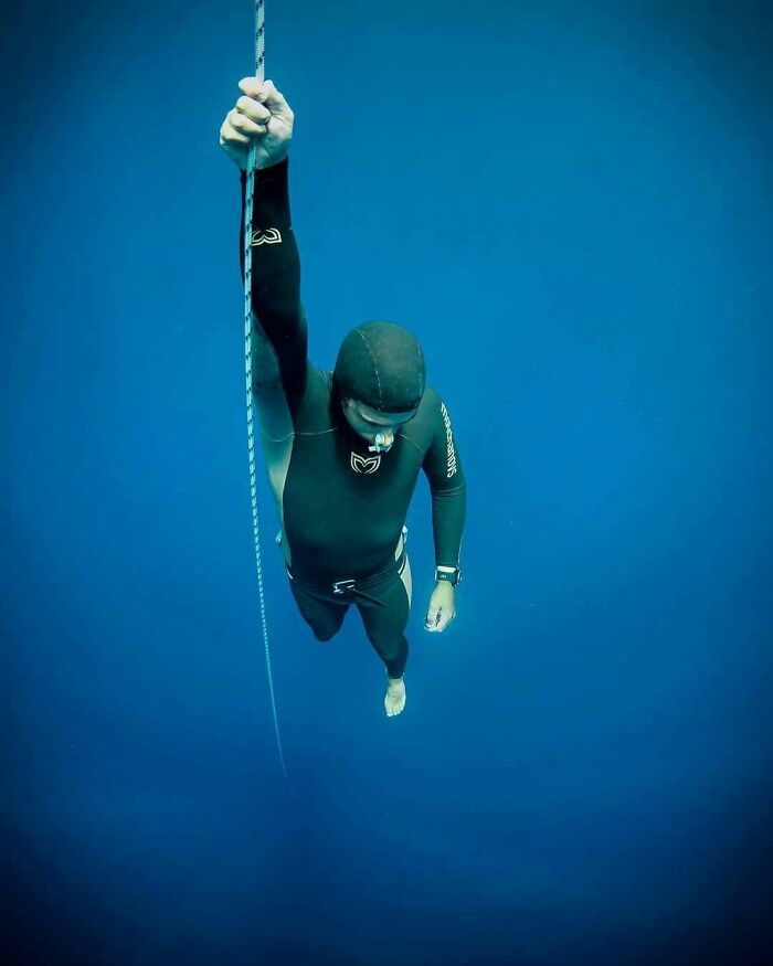 Uncomfortable water pics of a freediver descending into deep blue water, holding a rope. Makes you feel small.