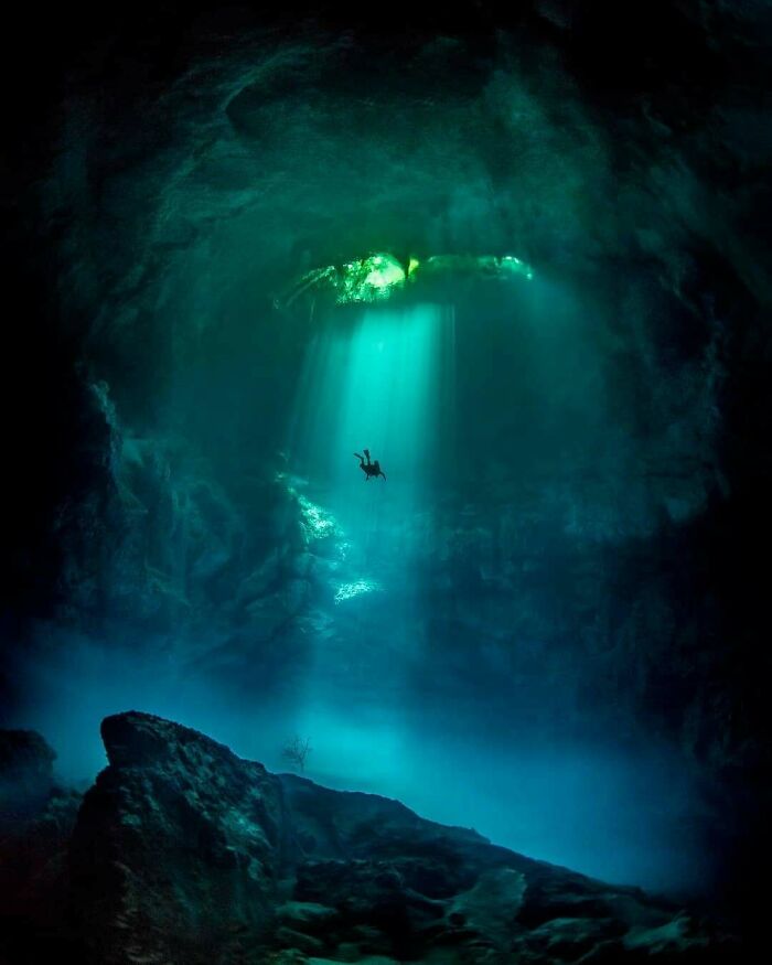 Unbelievable photos of a diver in a dark underwater cave, with brilliant light rays shining through. Feels like another universe.
