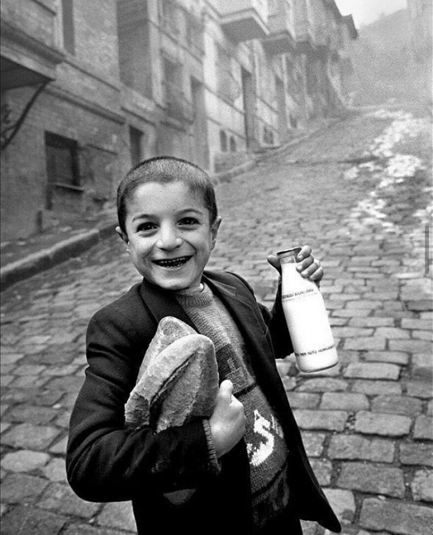 A smiling boy on a cobbled street, holding bread and milk, offering a glimpse into history through fascinating photos.