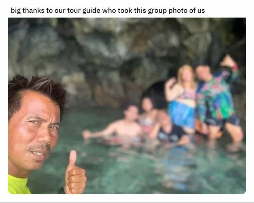 Tour guide giving thumbs up while a group poses in water near rocky cave, camping and hiking nature adventure.