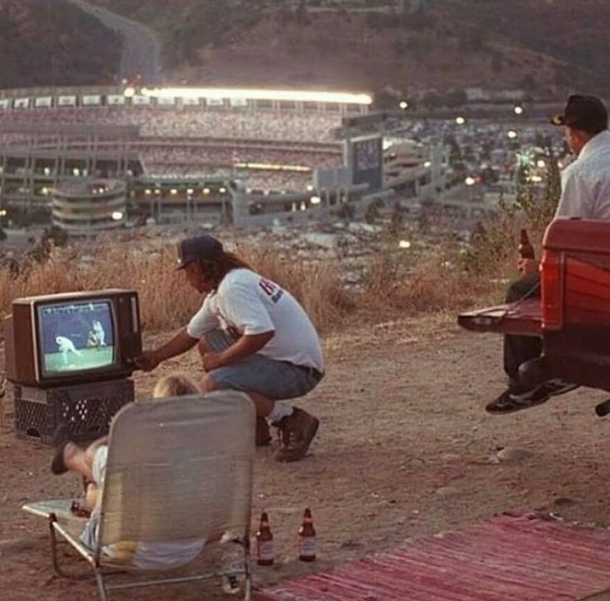 Friends watch a baseball game on a portable TV, overlooking a stadium at dusk, fascinating photos from history.