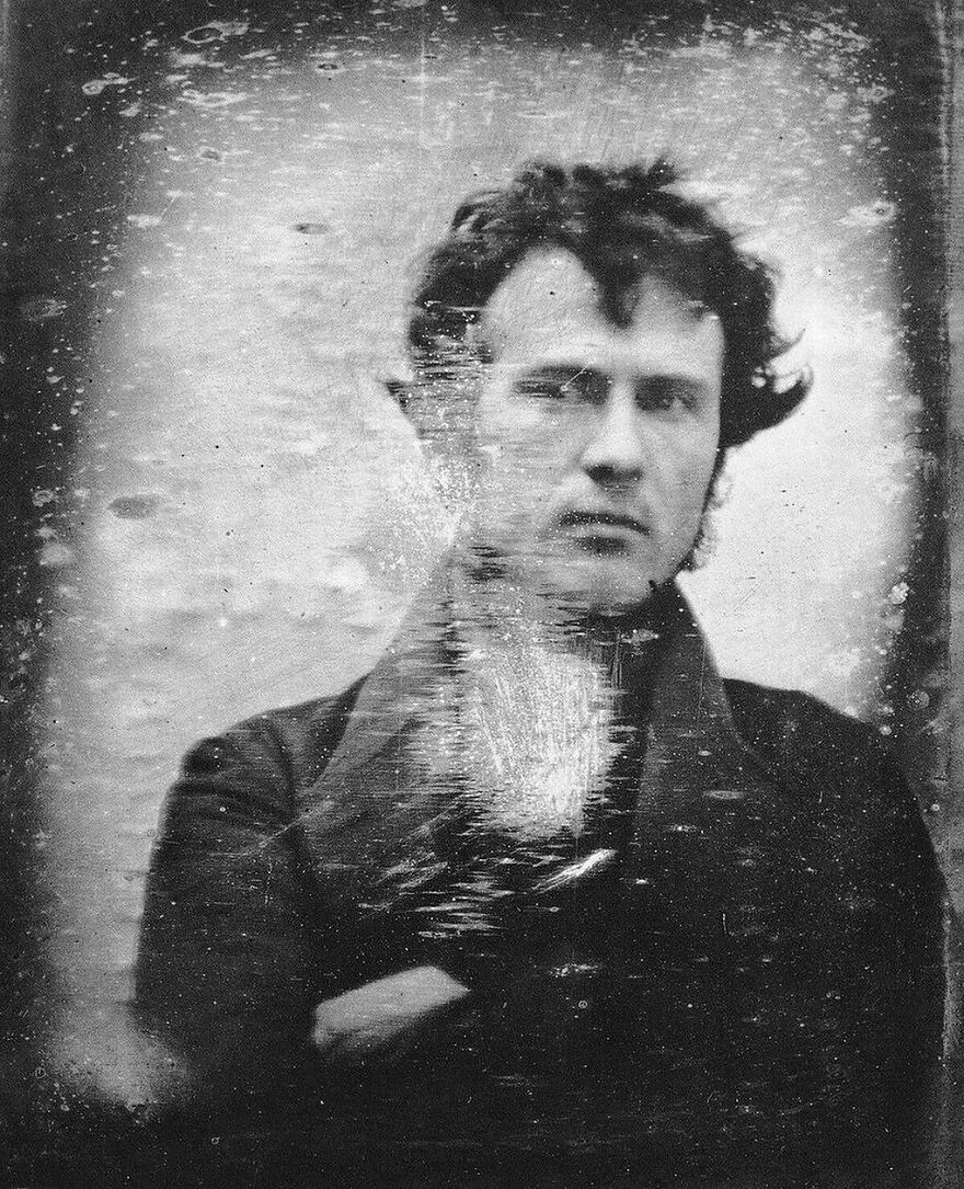 A scratched, faded black and white portrait of a man with dark, curly hair, teaching about history.