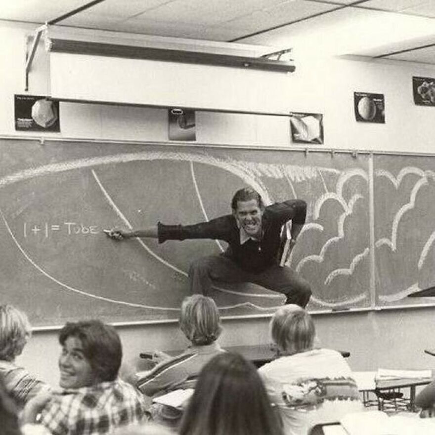 A passionate teacher demonstrates surfing on a blackboard, engaging students. A fascinating photo about history.