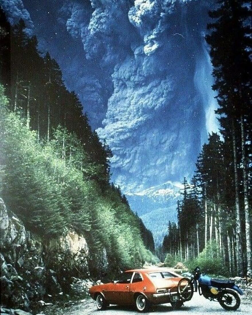Fascinating photo of a massive volcanic eruption plume towering over a mountain road with a car and motorcycle, offering a glimpse of history.