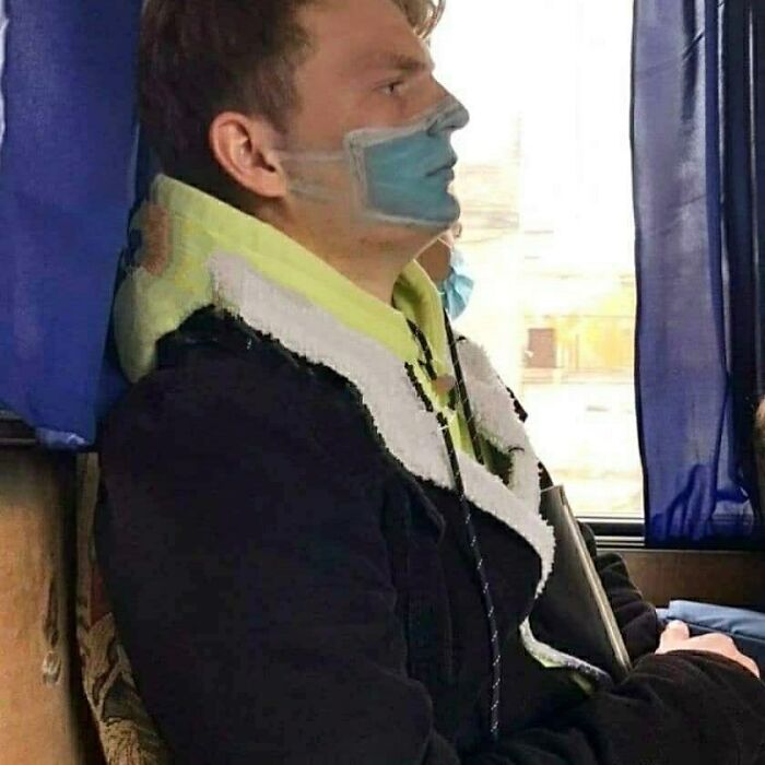 A man on a bus with a surgical mask painted on his face, a cursed image that amuses viewers.
