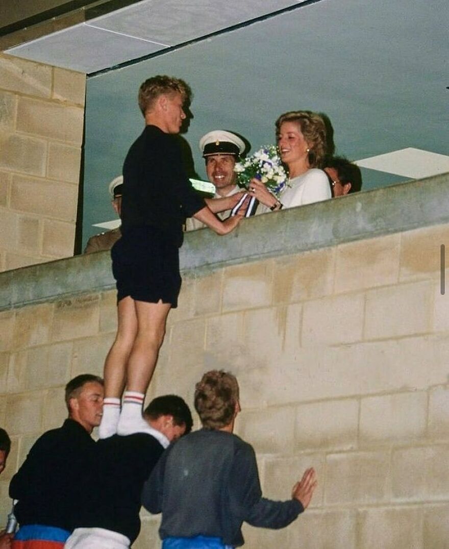 A man stands on friends' shoulders to hand flowers to Princess Diana, offering a fascinating photo of history.