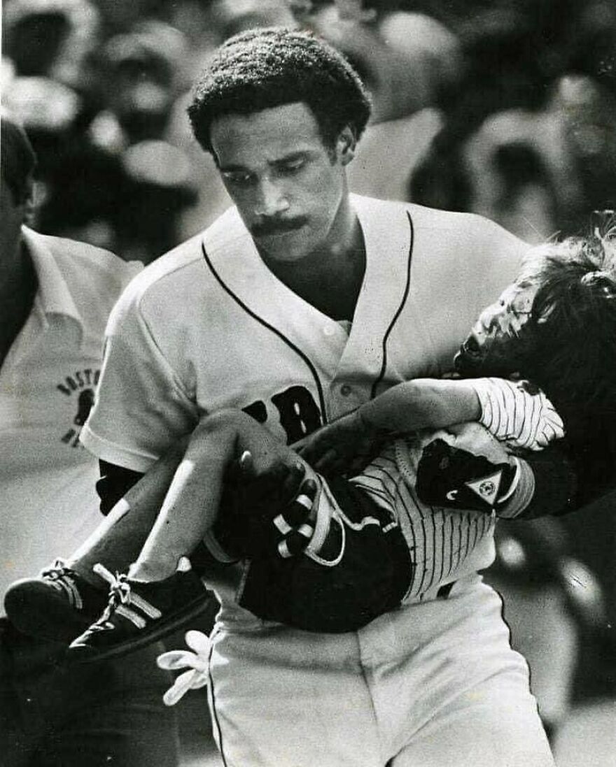 Black and white photo of a baseball player carrying a young child. Fascinating photos about history.
