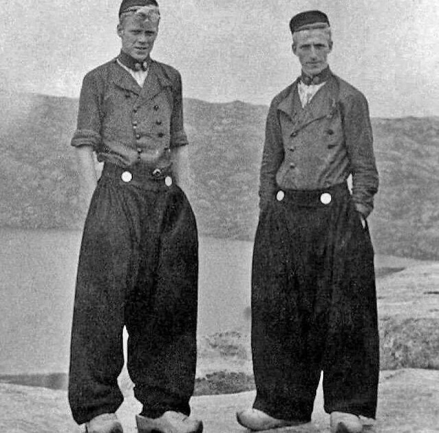 Two men in traditional attire, including wooden clogs and baggy pants, revealing fascinating photos of history.