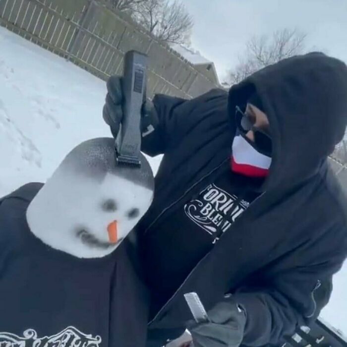 A person in a black hoodie and mask shaving a snowman's head, giving it a fresh haircut. A cursed image that confuses and amuses.