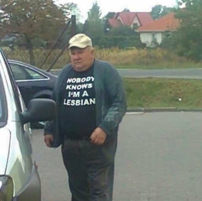 A man in a baseball cap and a t-shirt that reads "Nobody Knows I'm A Lesbian", a cursed image that confuses and amuses.