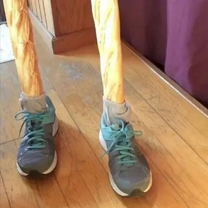 A cursed image of two baguette-like legs in socks and athletic shoes, standing on a wooden floor.