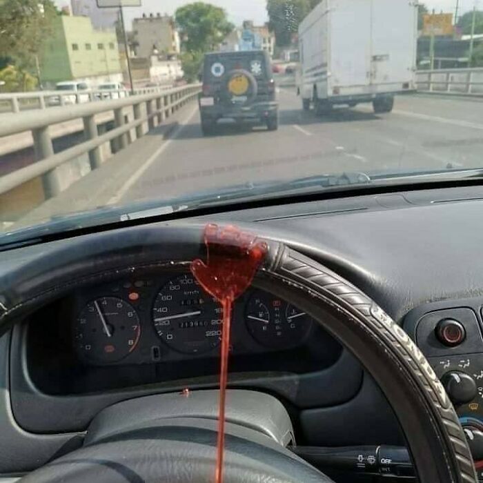 A melted red candy hand dripping onto a car dashboard, with traffic visible through the windshield, creating a cursed image.