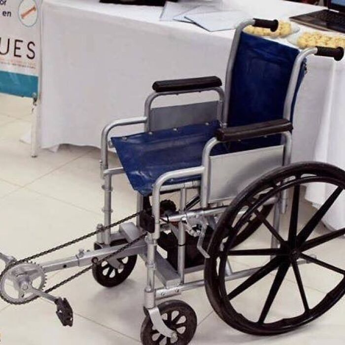 A cursed image showing a modified wheelchair with bike pedals attached to the front wheel, a confusing invention.