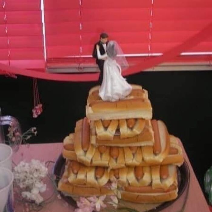 A wedding cake made of hot dogs, topped with a bride and groom figurine. A truly cursed image.