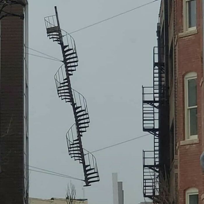 A cursed image of a floating spiral staircase between buildings against a grey sky, creating confusion.