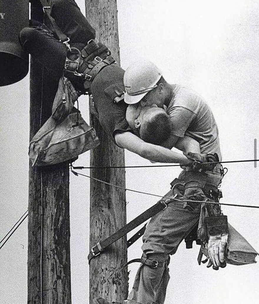 Fascinating photo of a lineman giving mouth-to-mouth resuscitation to another, saving a life; a part of history.