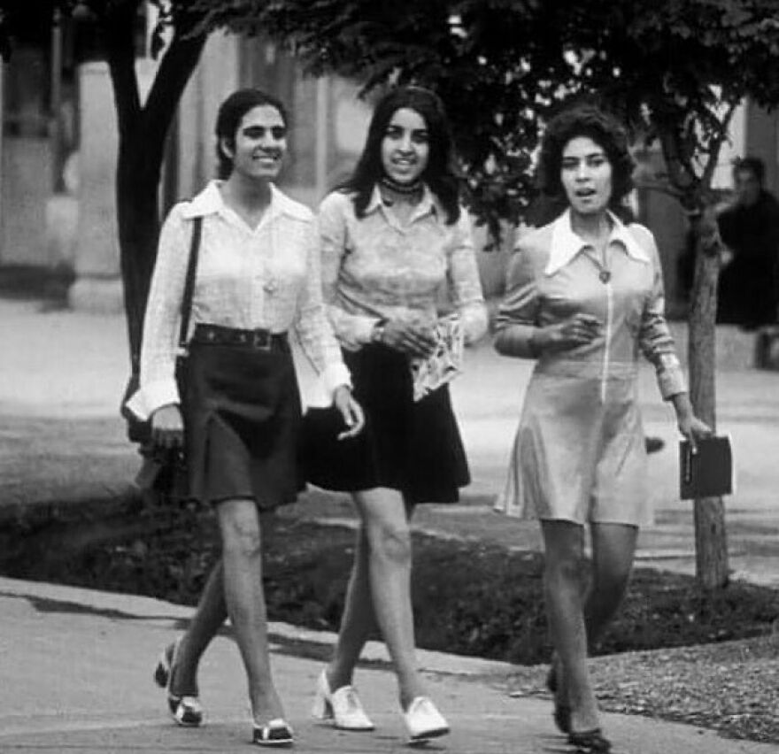 Three women in fashionable attire walking down a street, offering fascinating photos about history.
