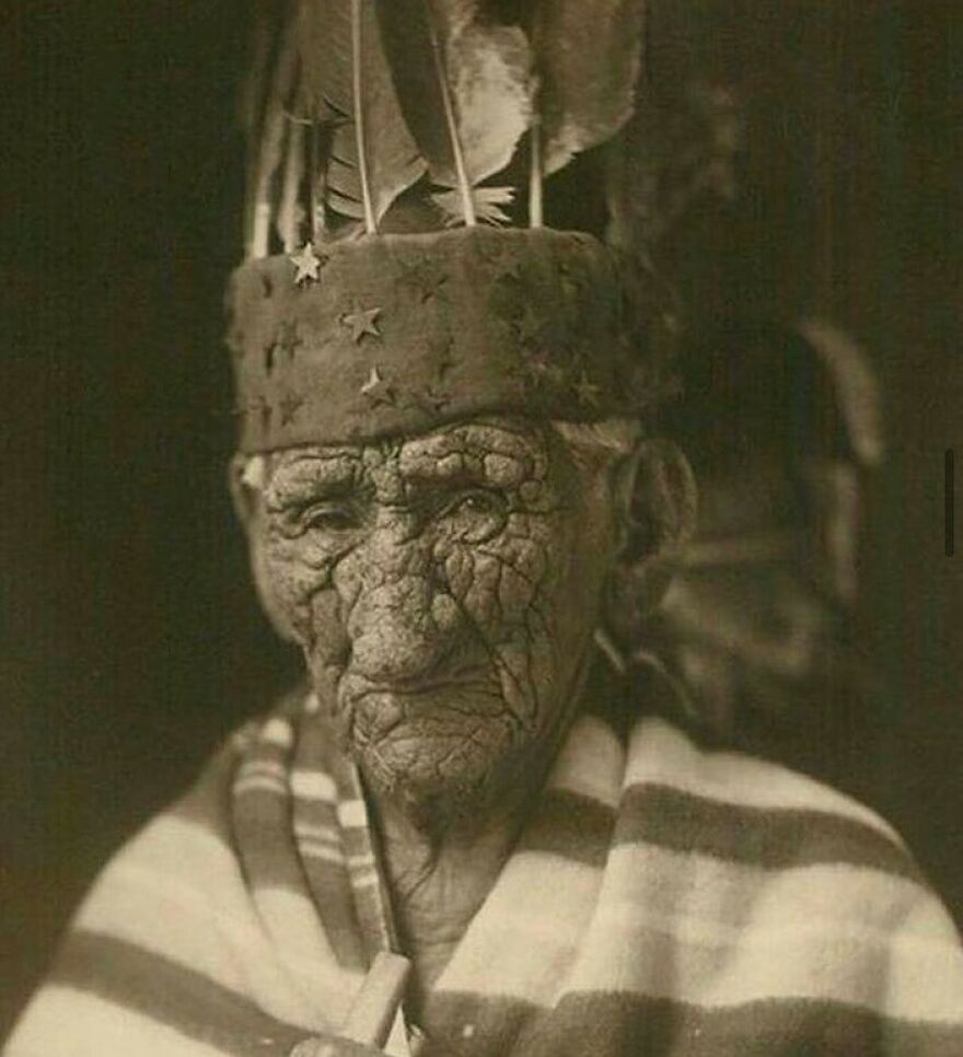 A vintage photo of an elderly person with deeply wrinkled skin and a feathered, star-decorated hat, offering fascinating photos of history.