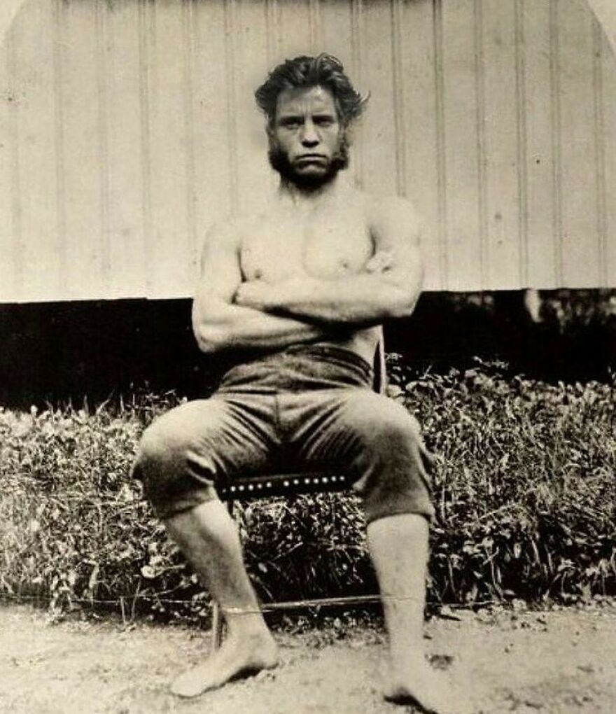 Old photo of a bare-chested man with a beard, arms crossed, teaching about history.