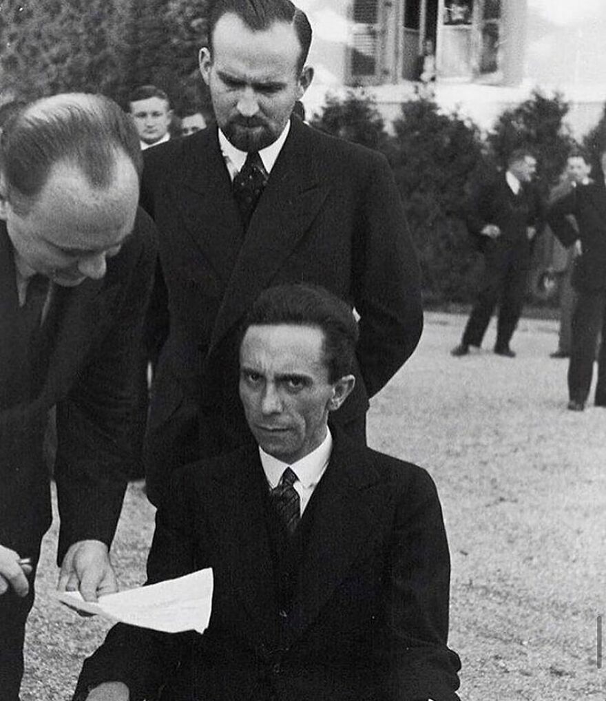 Joseph Goebbels, seated and looking at the camera, with other men in suits in the background. Fascinating photos about history.