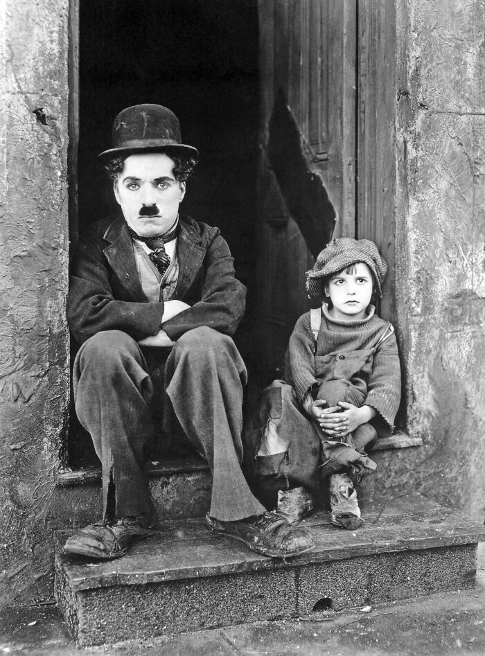 Black and white rare photo of a man in vintage clothing with a child sitting on stone steps from a past era.