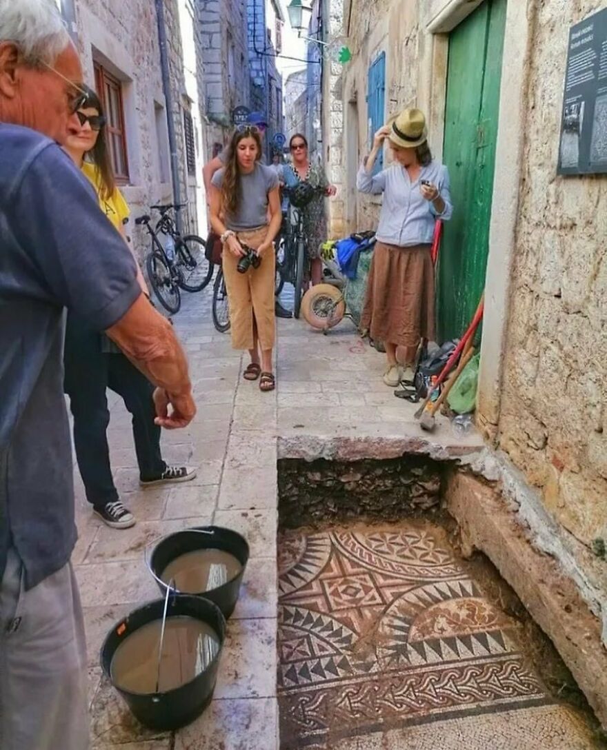 A group of people looking at an unearthed ancient mosaic floor in a narrow alley, revealing fascinating history.