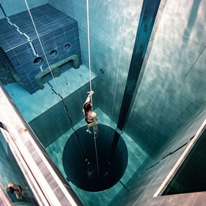 A person in a swimsuit descends into a deep, uncomfortable water pool, emphasizing feeling small.