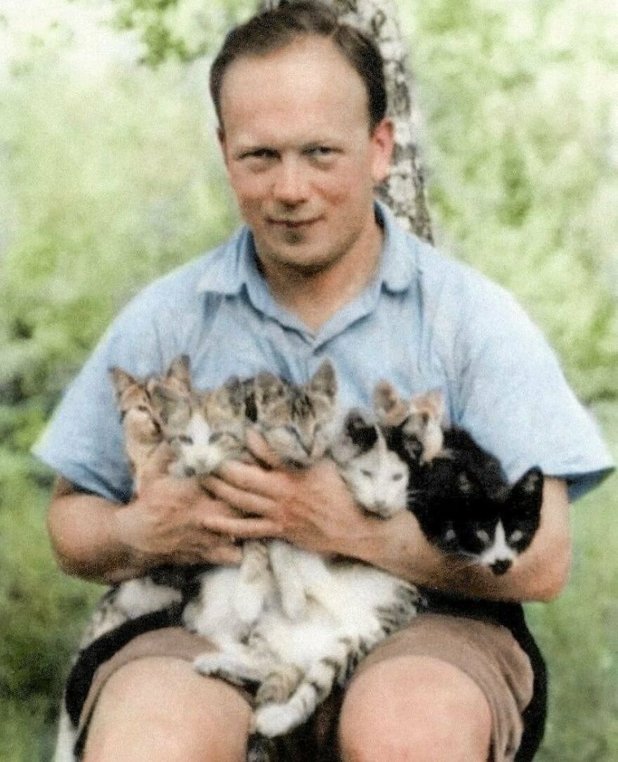 A man in a light blue shirt holding five kittens, with a tree and foliage in the background. Fascinating photos from history.