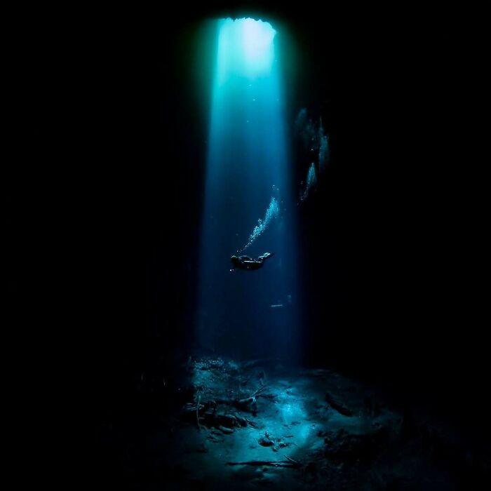 A lone diver descends into the dark, illuminated by a brilliant turquoise light beam from above. Uncomfortable water pics.