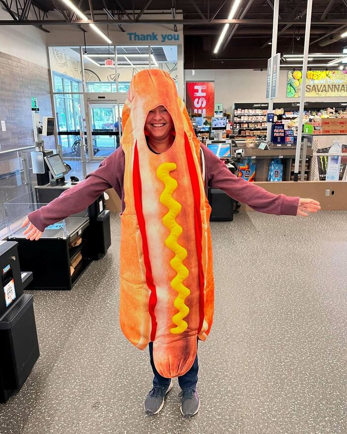 Person wearing a hot dog costume in a store, smiling with arms outstretched, illustrating gut warned feelings humorously.