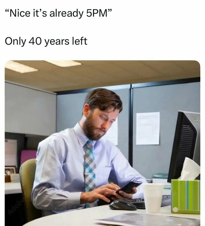 Man in office cubicle looking at phone with a tired expression, illustrating relatable adulthood memes about work life.